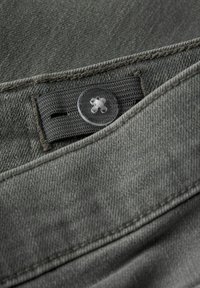 Tissu en denim gris avec un gros plan sur un bouton rond transparent et une ceinture texturée. Les coutures sont visibles le long des bords.
