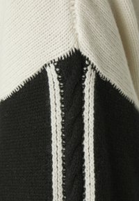 Maglione lavorato a maglia con un design a blocchi di colore crema e nero. Presenta cuciture testurizzate e strisce bianche verticali lungo le cuciture.