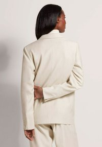 Beige gep tailored blazer gemaakt van zachte stof, met een enkele knoopsluiting, twee achterventilaties en vier knoopaccenten op de mouwen.