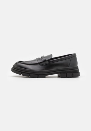 Black leather loafers with a smooth finish, featuring a front strap detail and a chunky rubber sole with grooved accents.