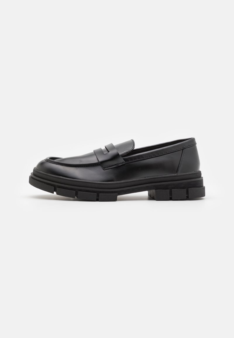 Mocassins de couro preto com um acabamento liso, apresentando um detalhe de tira na parte frontal e uma sola de borracha robusta com acabamentos estriados.