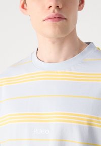 Hele sinine triibuline T-särk, millel on kollased horisontaalsed triibud, ringkaelusega ja valge broderi "HUGO" logo rinnal.
