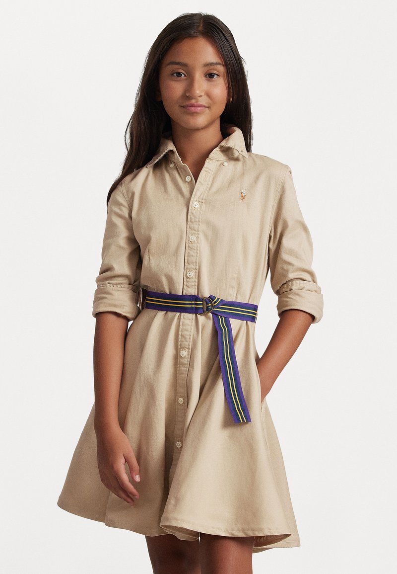 Μπεζ φόρεμα με κουμπιά και γυριστά μανίκια, με στενή μέση από ζώνη πολύχρωμης ρίγας. Διαθέτει κεντημένο λογότυπο στο πέτο.