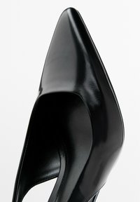 Svart läder högklackad sko med spetsig tå och slät yta. Har en öppen sidokutt-design för extra detalj.