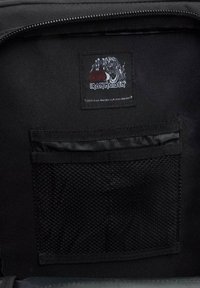 Svart tygväska med insida som har en stor nätficka. Utrustad med en sydd etikett med grafisk design och texten "Iron Maiden." Dragkedjestängning.