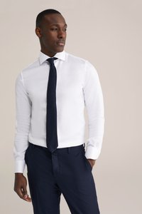 Witte overhemden met puntkraag, gecombineerd met donkerblauwe pantalon met krijtstreep en een bijpassende stropdas. Glad stof met een aansluitend ontwerp.