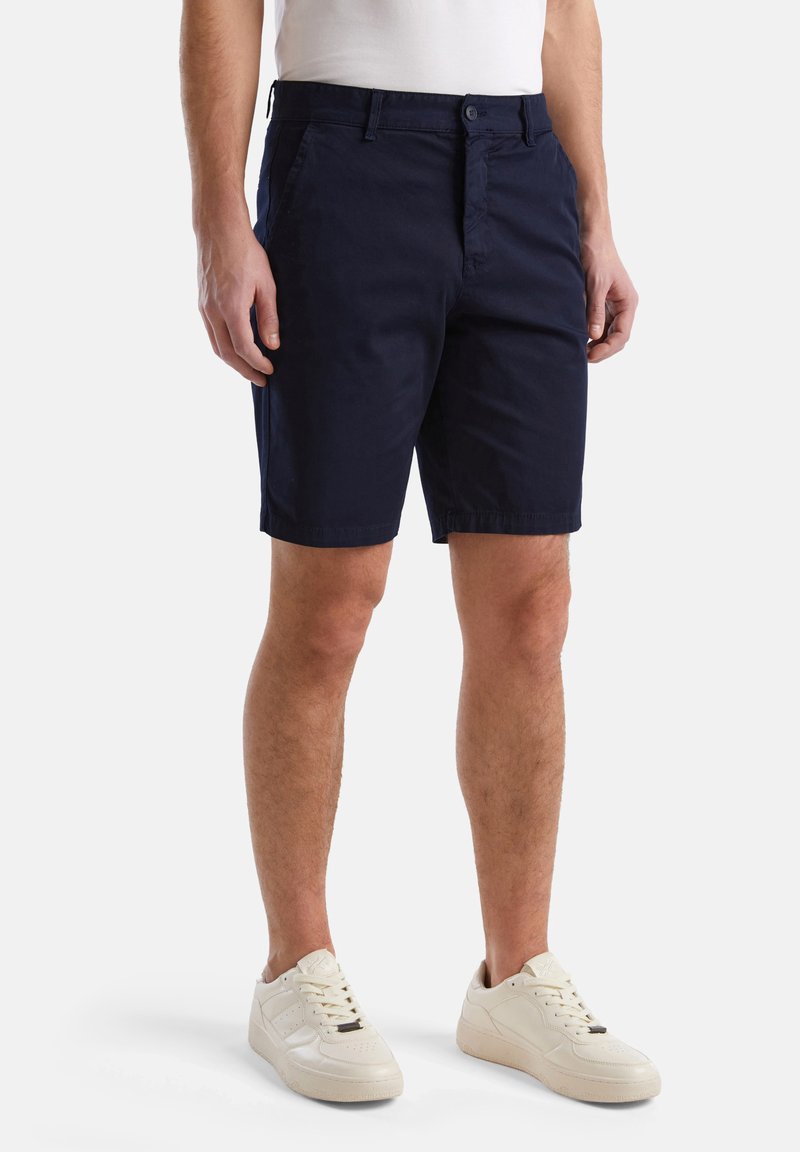 Shorts en coton bleu marine avec fermeture à bouton, poches latérales et coupe droite ; accompagnés de baskets couleur crème.