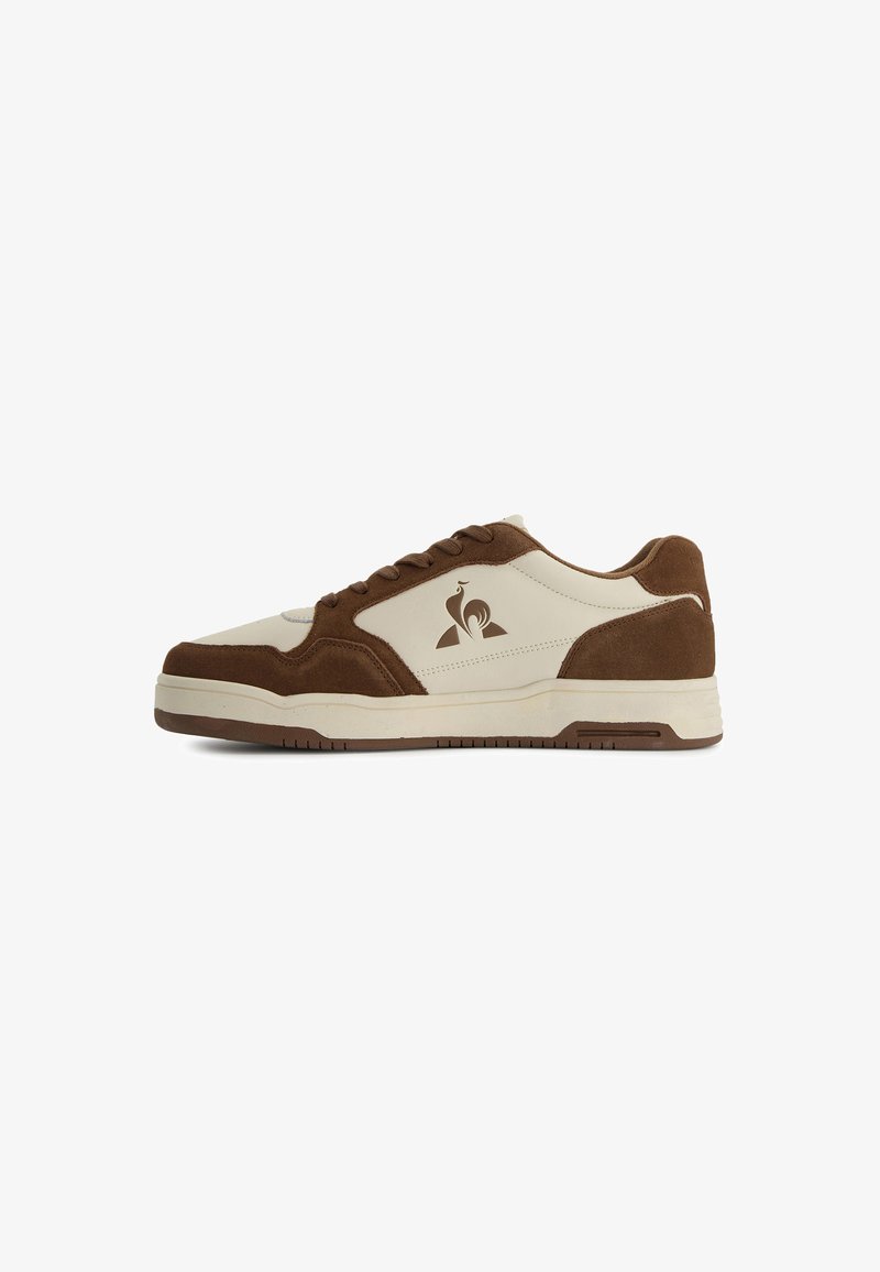 Sneaker met een beige leren bovenwerk en bruine suede accenten, ronde neus, vetersluiting en logo op de zijkant. Rubberen zool.