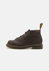 Brune lær ankle boot med gul stikning, rund tå, fem øjenlåg og en sort hæl. Har en trækkrog med mærkelogo.