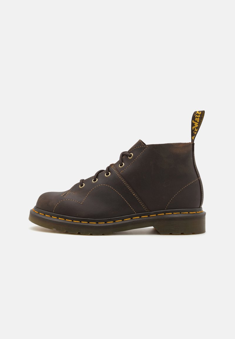 Brune lær ankle boot med gul stikning, rund tå, fem øjenlåg og en sort hæl. Har en trækkrog med mærkelogo.