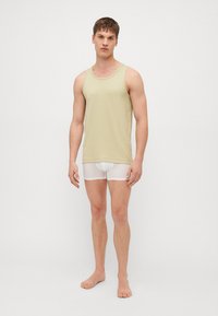 Débardeur vert clair ajusté avec un col arrondi, associé à un short blanc. Le haut est lisse et le short est semi-transparent.