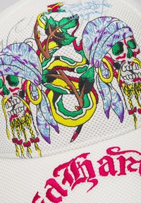 Cappello bianco con texture che presenta teschi ricamati colorati con accenti decorativi, un serpente verde e motivi intricati. La parola "Faith" in corsivo rosa.