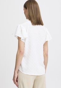 Blusa bianca a maniche corte con maniche a volant, tessuto testurizzato con piccoli motivi circolari e orlo arrotondato.