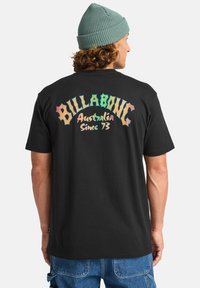 Black t-shirt featuring colorful, stylized text on the back that reads "BILLABONG Australia Since 73." Cotton material, short sleeves.