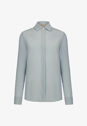 Blouse pour femme à manches longues gris clair avec col pointu, patte de boutonnage cachée, et un seul bouton visible en haut.