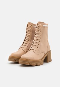 Botines beige con un upper texturizado, diseño de cordones, ojales dorados y una suela de tacón grueso con un dibujo en la tracción.