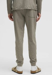 Lysegrå sportbukser med slim fit, tapered manchetter, en baglomme og blød tekstur, parret med beige slip-on sko og hvide sokker.