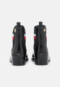 Bottines en cuir verni noir avec panneaux latéraux élastiques, présentant des accents rayés rouge, blanc et bleu ainsi que des attaches dorées à l'arrière.