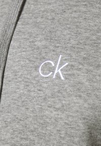 Pilkas džemperis su minkšta medžiaga, su mažu balta siuvinėta "ck" logotipu krūtinėje. Lygi tekstūra su laisvu pjūviu.