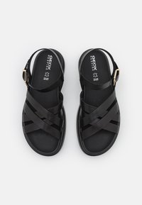Sandali neri con suola in gomma, caratterizzati da cinturini incrociati e una fascia regolabile sul retro. Texture liscia con perforazioni sulla soletta.