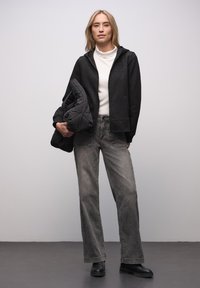 Czarna bluza z kapturem z błyszczącymi detalami, biały golf i szare szerokie dżinsy. Zestaw uzupełniają czarne botki za kostkę.