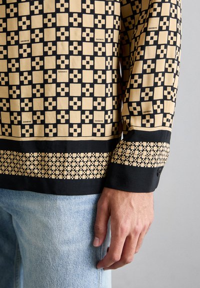 Langarmshirt met een zwart en beige geometrisch patroon, met een gladde textuur, knoopmanchetten en contrasterende zoomdetails.