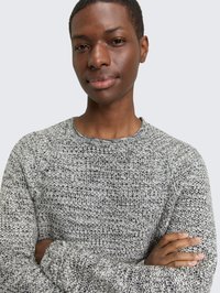 Grauer, strukturierter Strickpullover mit rundem Ausschnitt und Raglanärmeln. Der Stoff zeigt ein gemischtes Muster aus dunklen und hellen Fäden.