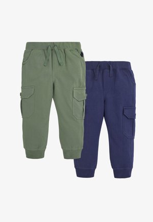 Małe dziecko w koszulce w paski z nadrukiem traktora trzyma białą miskę do mieszania ze szpatulką w pomieszczeniu.