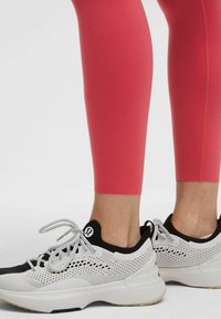 Leggings roz până la gleznă asortați cu pantofi sport negri și albi, având detalii din plasă și talpă texturată.