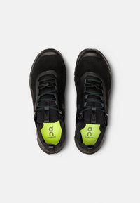 Baskets de course noires avec une tige en mesh, une surface texturée et une semelle intérieure verte contrastante. Elles sont équipées d'un système de laçage sécurisé et d'un embout renforcé.