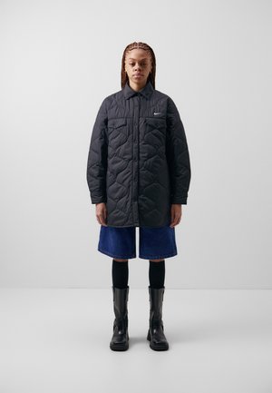 Veste noire matelassée avec un devant à boutons, deux poches poitrine et un petit logo. Associée à un short en jean, des leggings noirs et des bottines noires.