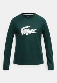 Camiseta de algodón verde de manga larga con un gráfico blanco de cocodrilo en el frente, cuello redondo y ajuste estándar. Textura simple y suave.