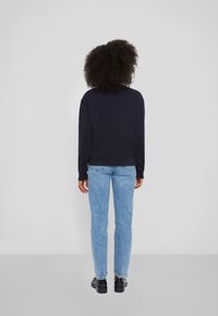 Marinblå sweatshirt med rund halsringning, med lång ärm och ribbade muddar, tillsammans med ljusblå, slim-fit jeans och svarta skor.