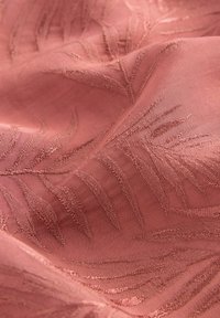 Texturerad, rosa tyg med ett subtilt bladmönster; slät, vävd yta med upphöjd broderade detaljer i en matchande nyans.