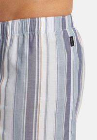 Pantaloni corti a righe in cotone di colore azzurro chiaro, blu navy e bianco. Vita elastica con una piccola etichetta del marchio sul lato. Texture morbida e design casual.