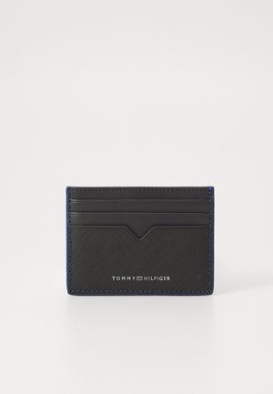Black leather cardholder with blue stitching. Features multiple card slots and a raised design at the top. Logo displayed at the bottom.