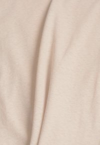 Tissu beige doux en gros plan montrant une texture lisse et des plis délicats.