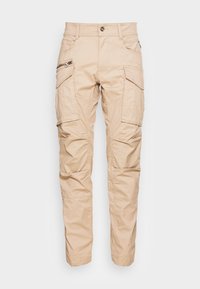 Beige cargo bukser lavet af slidstærkt stof, med flere lommer, lynlåsdetaljer og et let affaset bendesign.