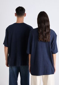 Camisetas de manga corta en azul marino de gran tamaño, fabricadas en tejido suave, exhibidas en un modelo masculino y una modelo femenina vistas desde atrás.
