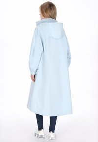 Világoskék vízálló kabát kapucnival, hosszú ujjakkal és elasztikus mandzsettákkal, lazább szabással, középvádli hosszúságig ér.
