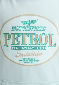 Minzgrüner Stoff mit einem großen Grafikdesign, das "PETROL" in fettem Grün und Gold zeigt. Enthält "MOTORWORKS" und kleinere Textdetails.
