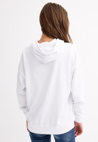 Sudadera blanca con capucha, de corte relajado, mangas largas y puños acanalados. Cuenta con un bolsillo canguro y una textura de tela suave.