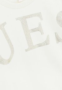 Tessuto bianco con grandi lettere "U E" create da piccoli chiodini d'argento disposti in un motivo decorativo.