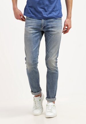 Jeans ajustados de un azul claro en denim desgastado, con puños enrollados. Combinados con zapatillas blancas con acentos verdes. Camiseta azul lisa llevada encima.