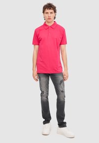 Camisa polo fucsia de manga corta, con cuello y tapeta de tres botones, combinada con jeans grises desgastados y zapatillas blancas.