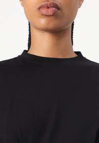 Černé bavlněné tričko s vysokým výstřihem a krátkými rukávy, hladkou texturou a minimalistickým designem.