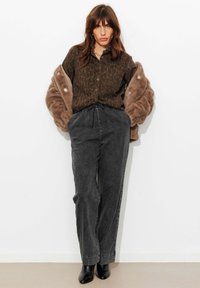 Chemise à boutons imprimé léopard marron, pantalon large en denim gris, et bottines noires. Veste en fausse fourrure marron clair posée sur les épaules.