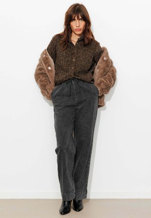 Chemise à boutons imprimé léopard marron, pantalon large en denim gris, et bottines noires. Veste en fausse fourrure marron clair posée sur les épaules.