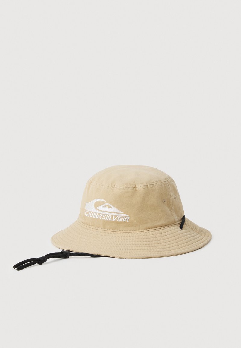 Beżowy kapelusz typu bucket wykonany z bawełny, z szerokim rondem, regulowanym paskiem pod brodą oraz białym logo Quiksilver z przodu.
