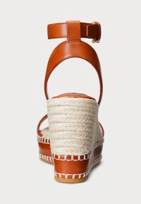 Sandalo in pelle marrone con tacco a zeppa in corda di espadrillas. Presenta una fascia alla caviglia con fibbia e dettagli a punto in contrasto.